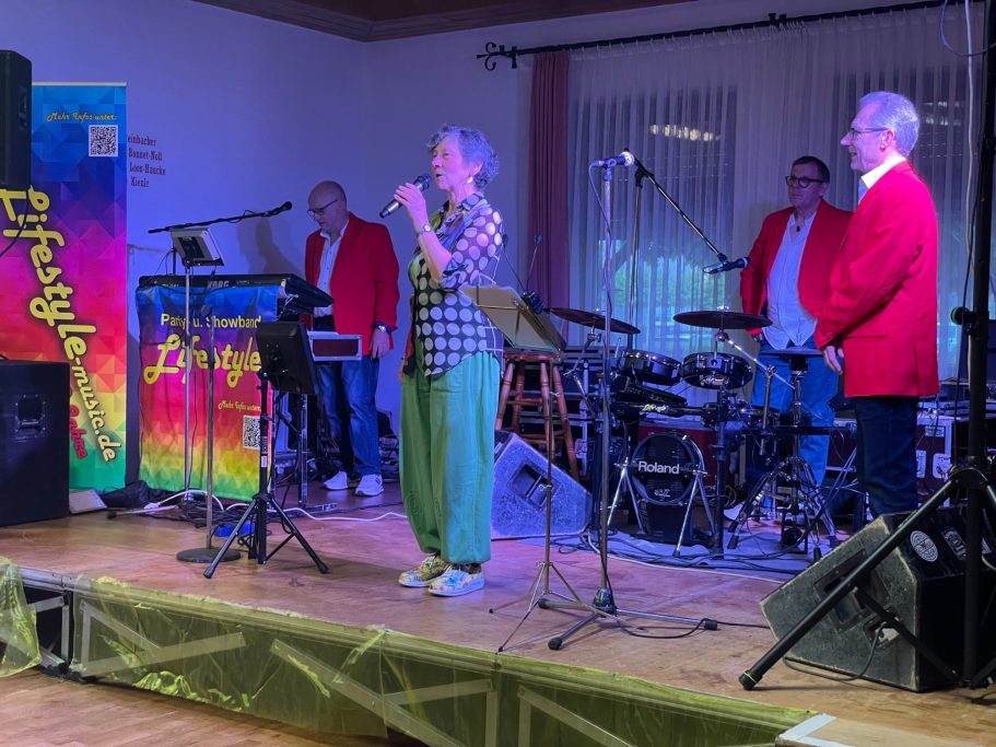 Vereinsvorsitzende des MGV Lingenfeld, Annette Kienle, hält Ansprache an Gäste der Veranstaltung auf der Bühne bei der Band